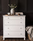 White dresser with decorative items against a dark paneled wall
